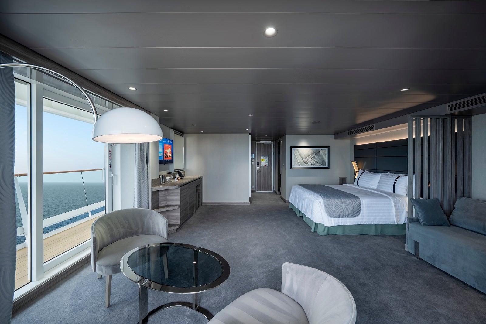 A large cruise ship cabin with gray decor and a bed, table and chairs