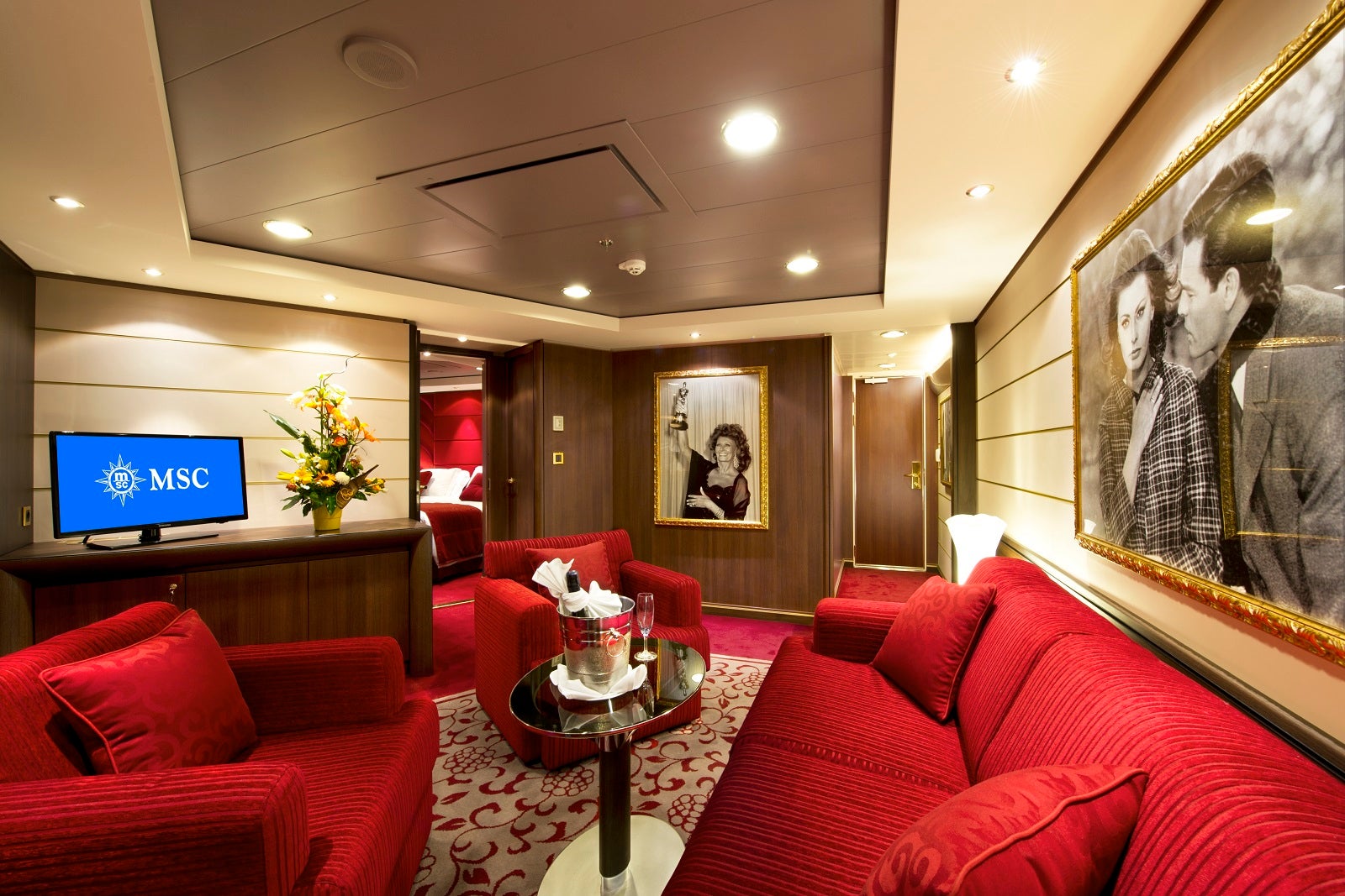 A cruise ship cabin with bright red chairs and a sofa, with black and white photos on the walls
