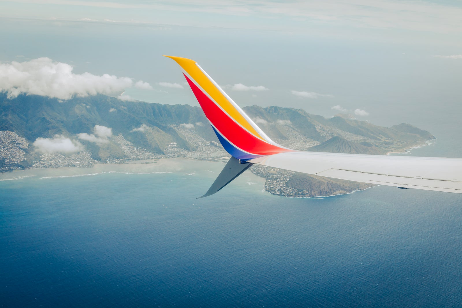 the wing of a Southwest Airlines plane is seen from the plane window, flying over a lake and mountains