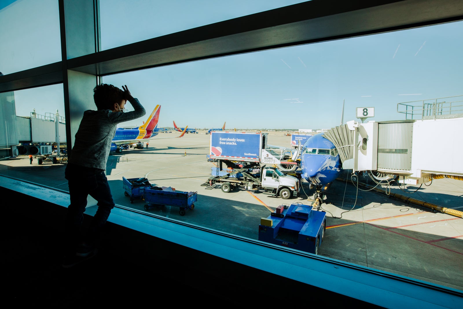 a child looks out the window of an airport, looking at a Southwest Airlines plane parked at a gate