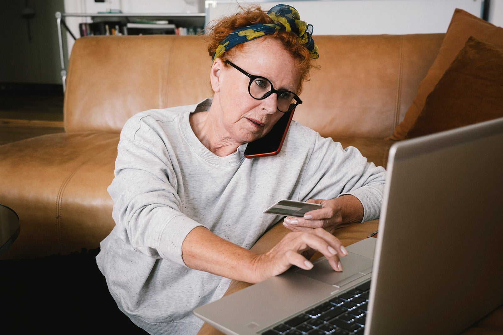 Senior woman talking on smartphone while paying online via laptop