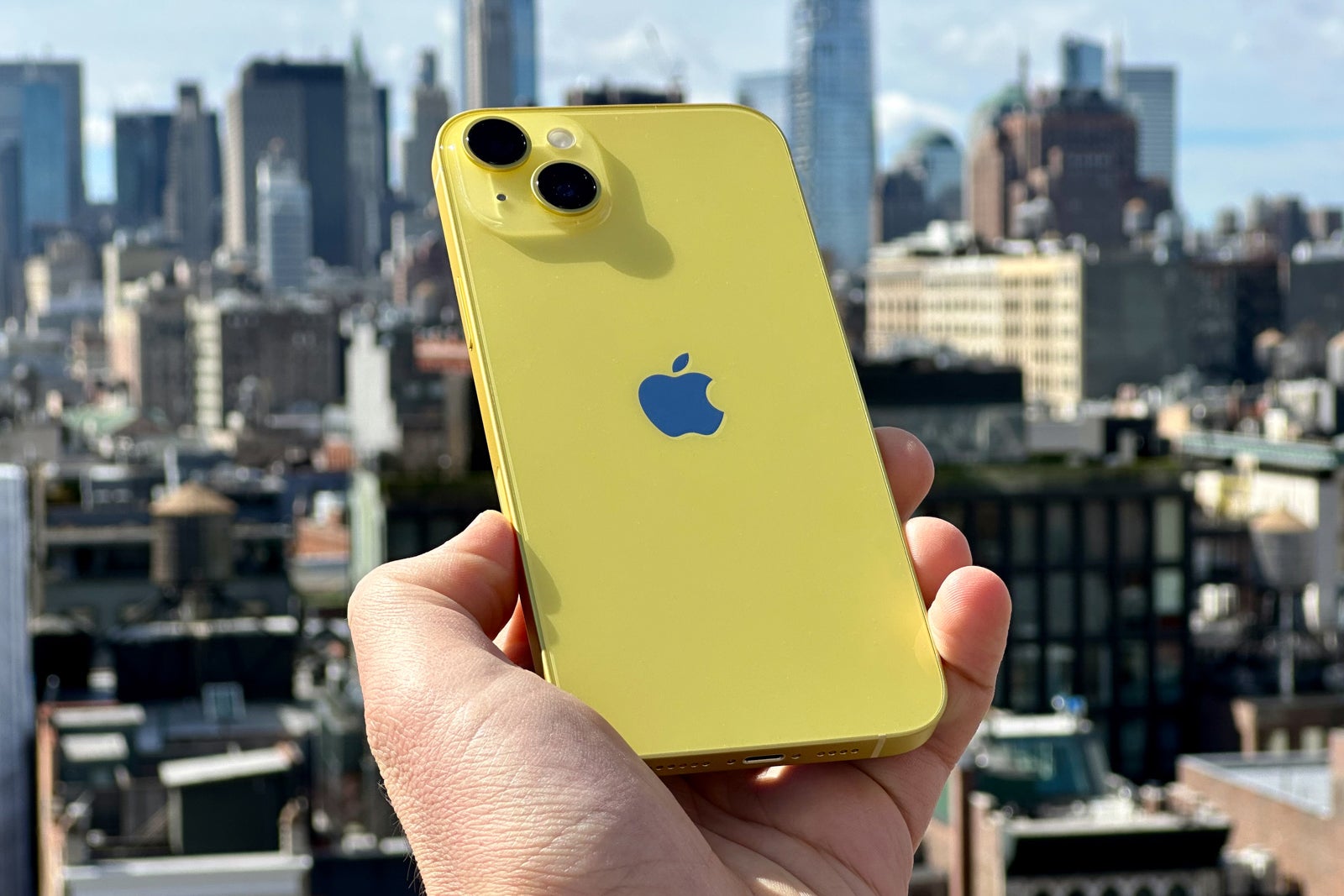 A hand holds a yellow iPhone with city buildings in the background