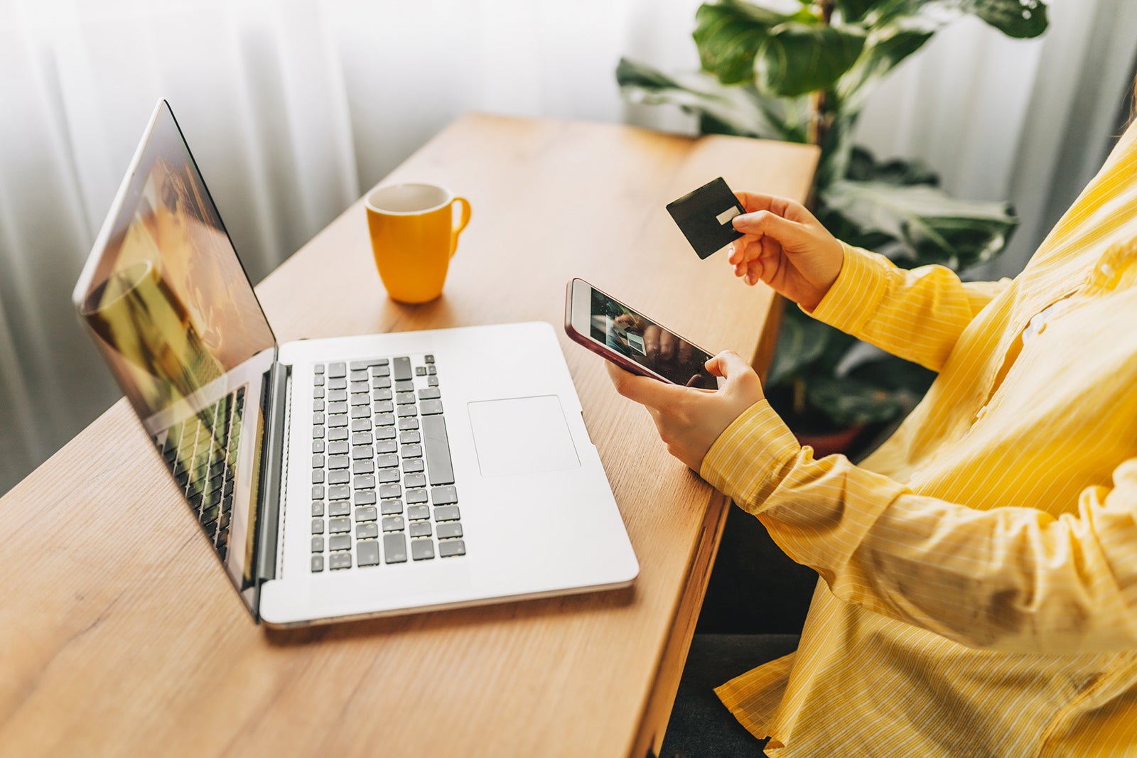 an unseen person sits at a computer holding a smartphone and credit card