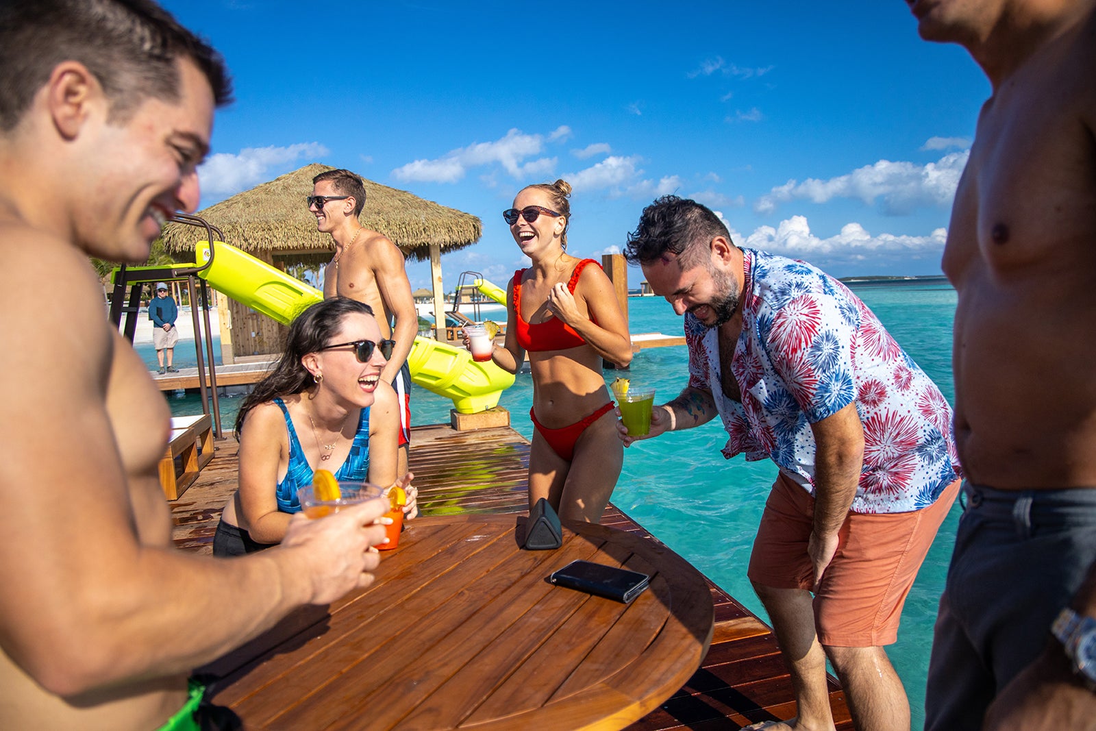 Young adults in swimsuits laughing and drinking on floating cabana at Bahamian island