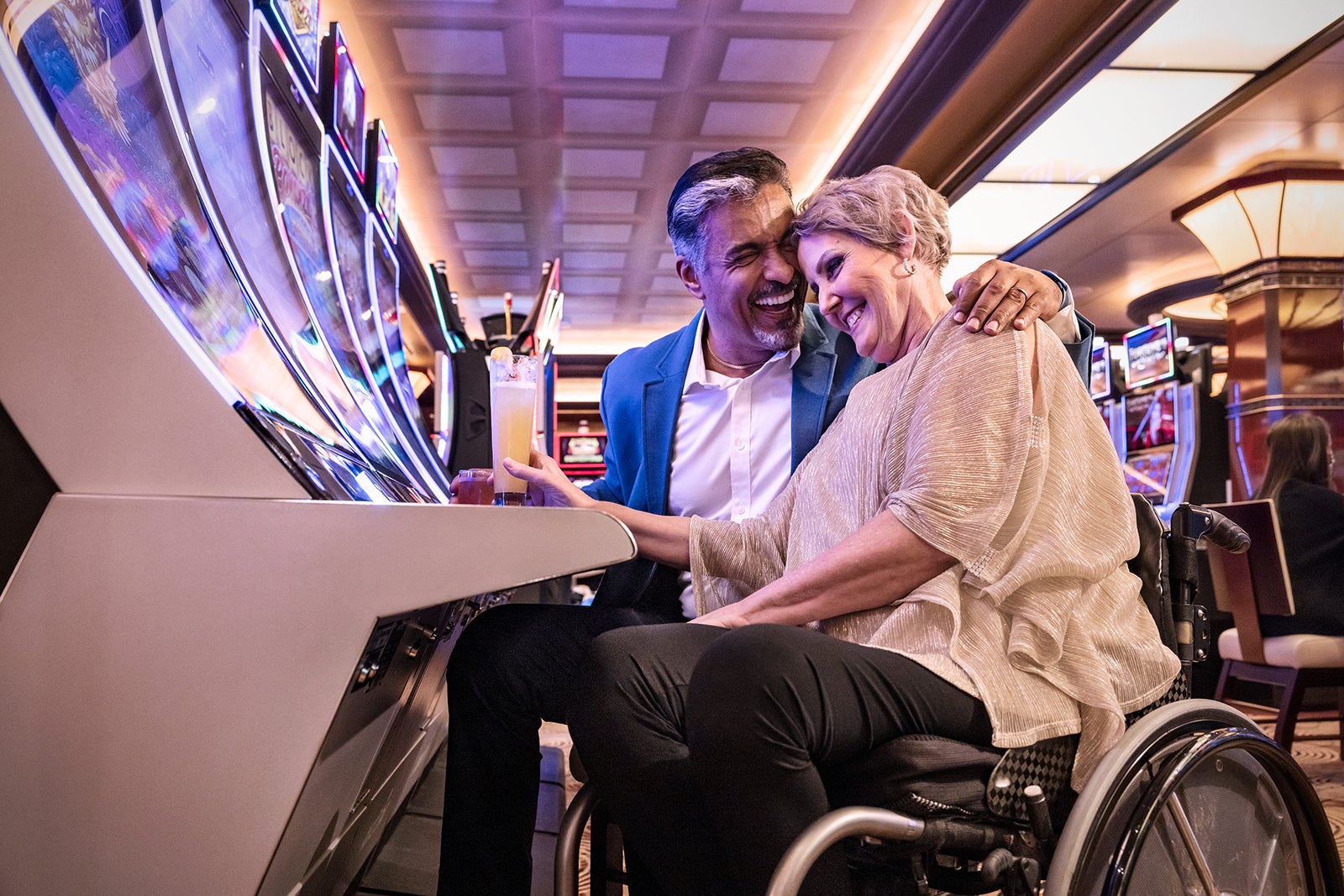 Older woman in wheelchair and older man with drinks at slot machines on a cruise ship