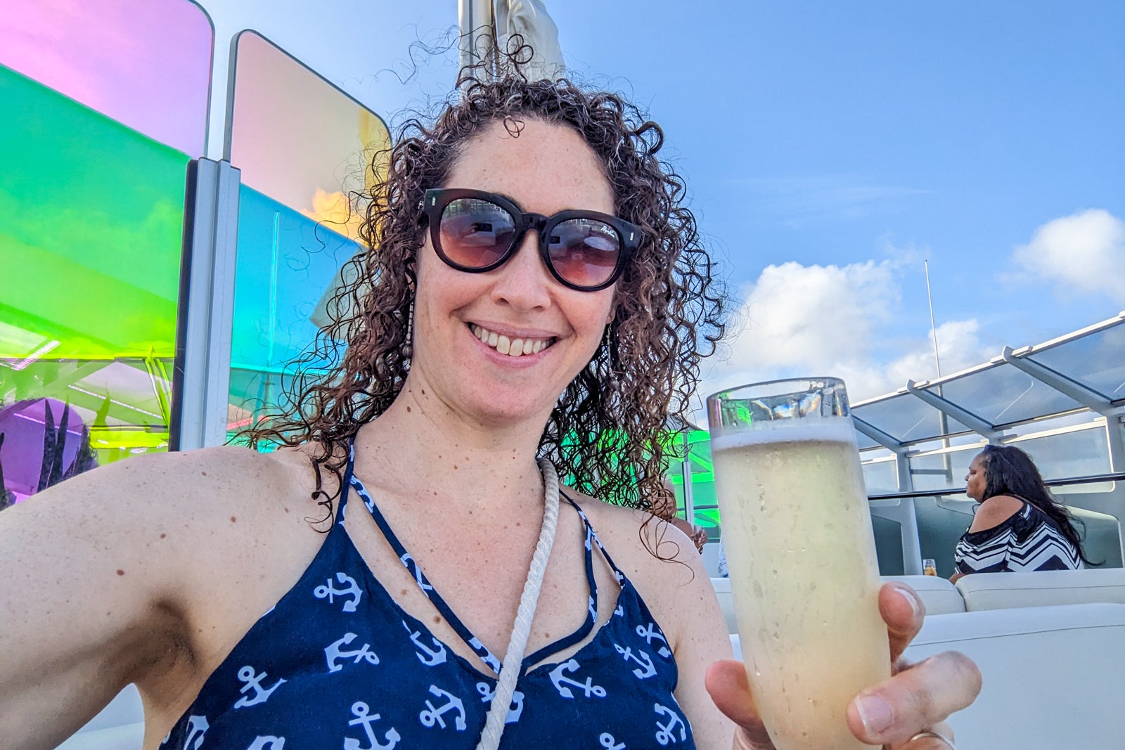 Woman in sunglasses and blue top with anchors drinking champagne