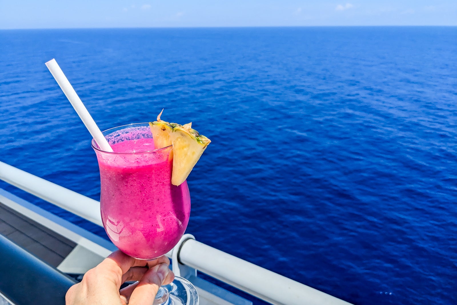 Bright magenta smoothie by cruise ship railing overlooking the ocean