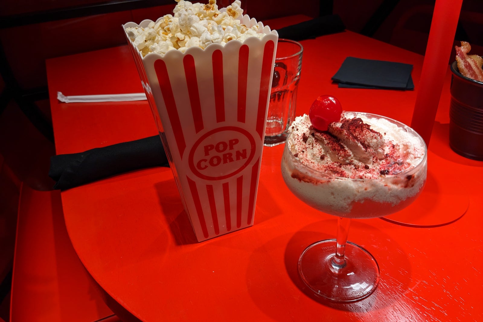 Two drinks on a red table, one in a container that looks like a popcorn bag