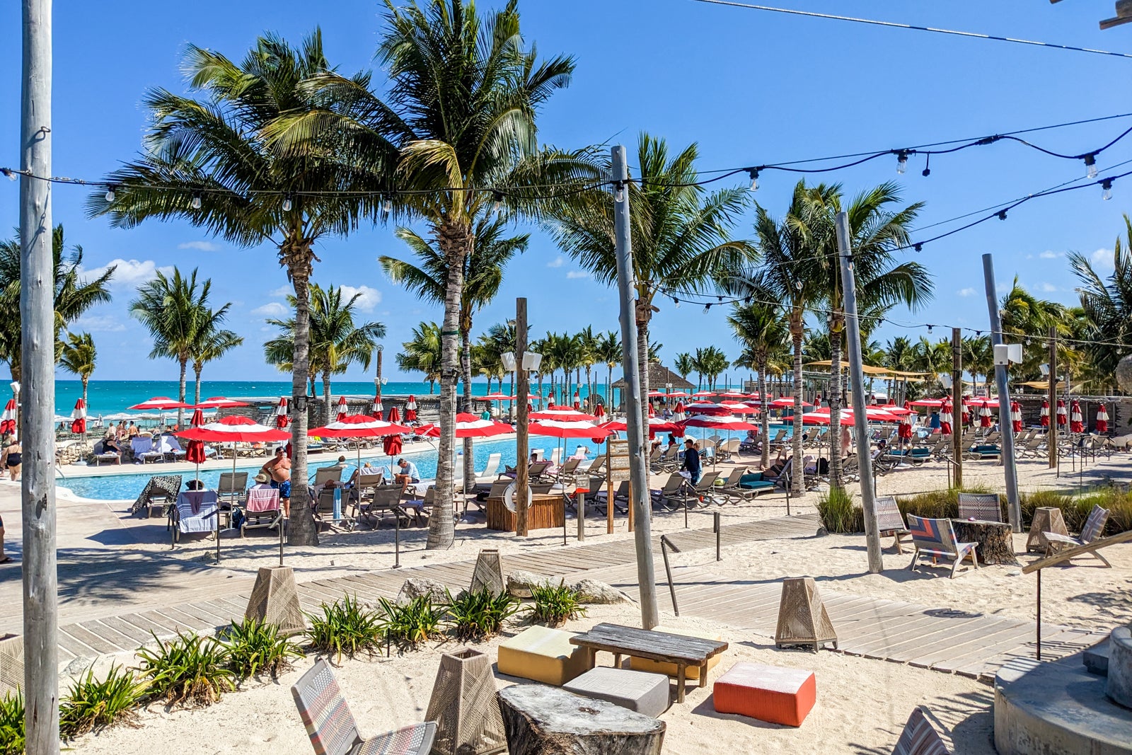 Pool surrounded by red umbrellas on a palm tree lined beach