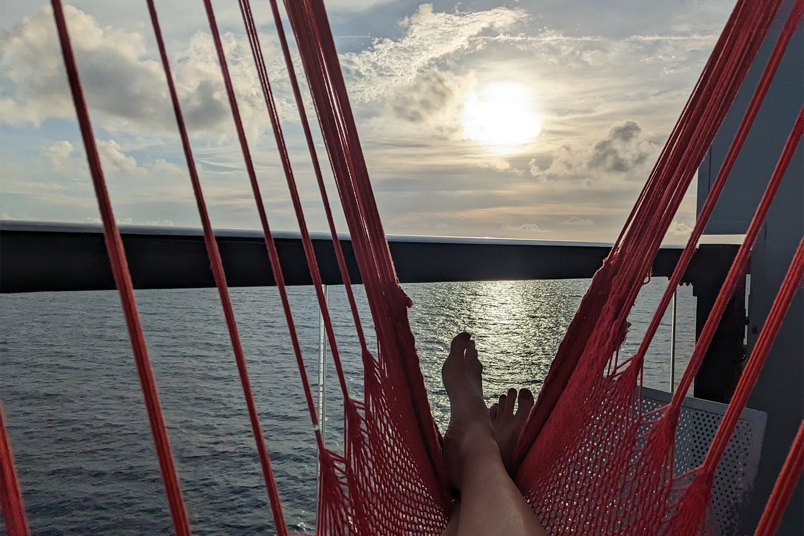 Feet on red hammock looking over sea and sunrise