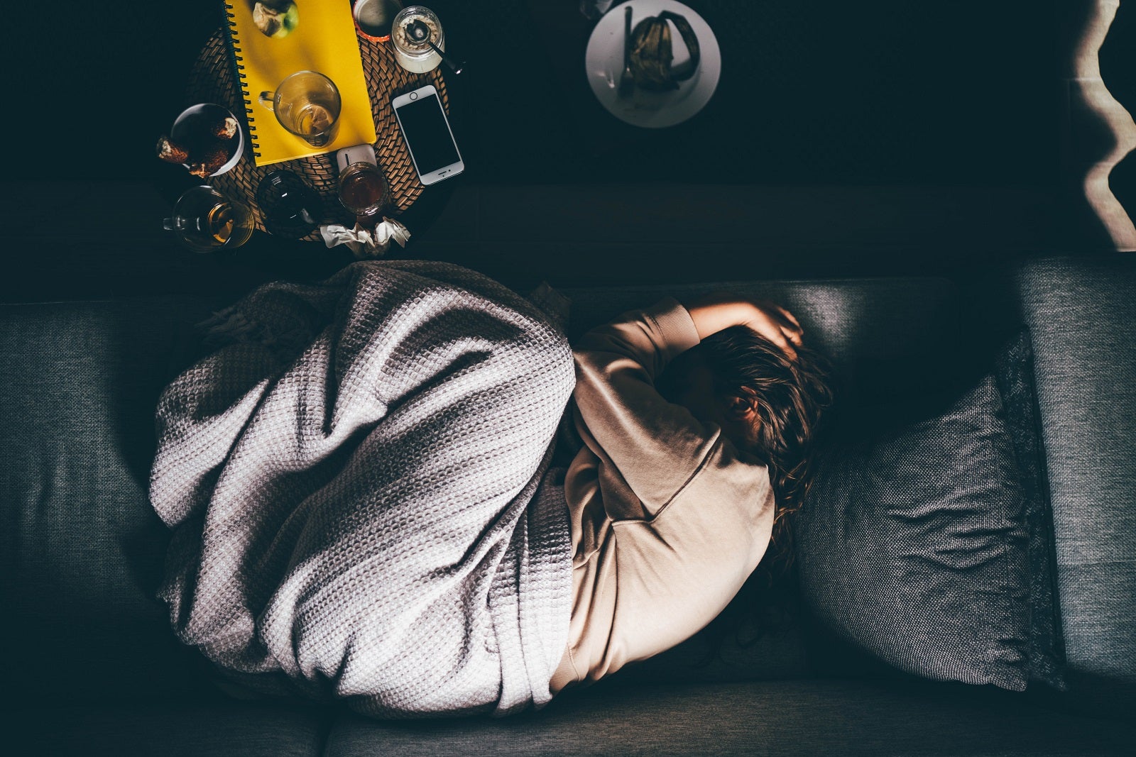 Overheard shot of a sick person curled up on a sofa with a blanket