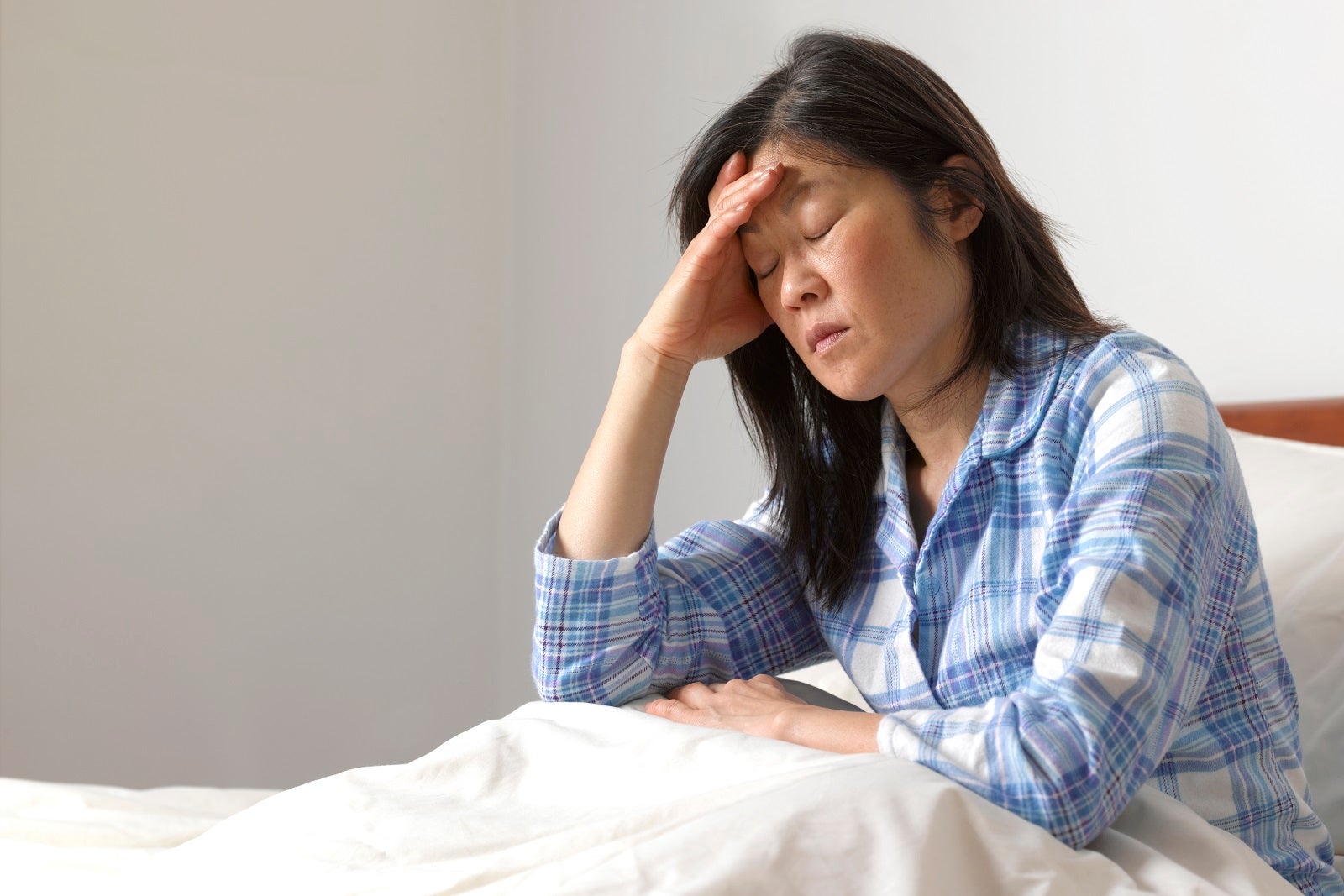 Woman sick in bed, sitting up and holding her head
