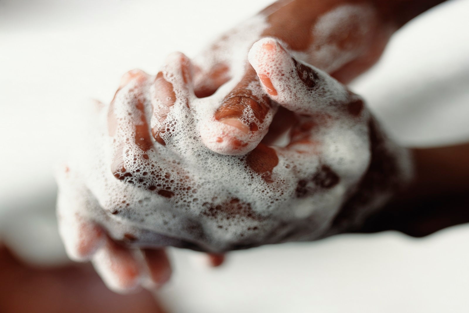 A close-up of two soapy hands being rubbed together as someone is washing them