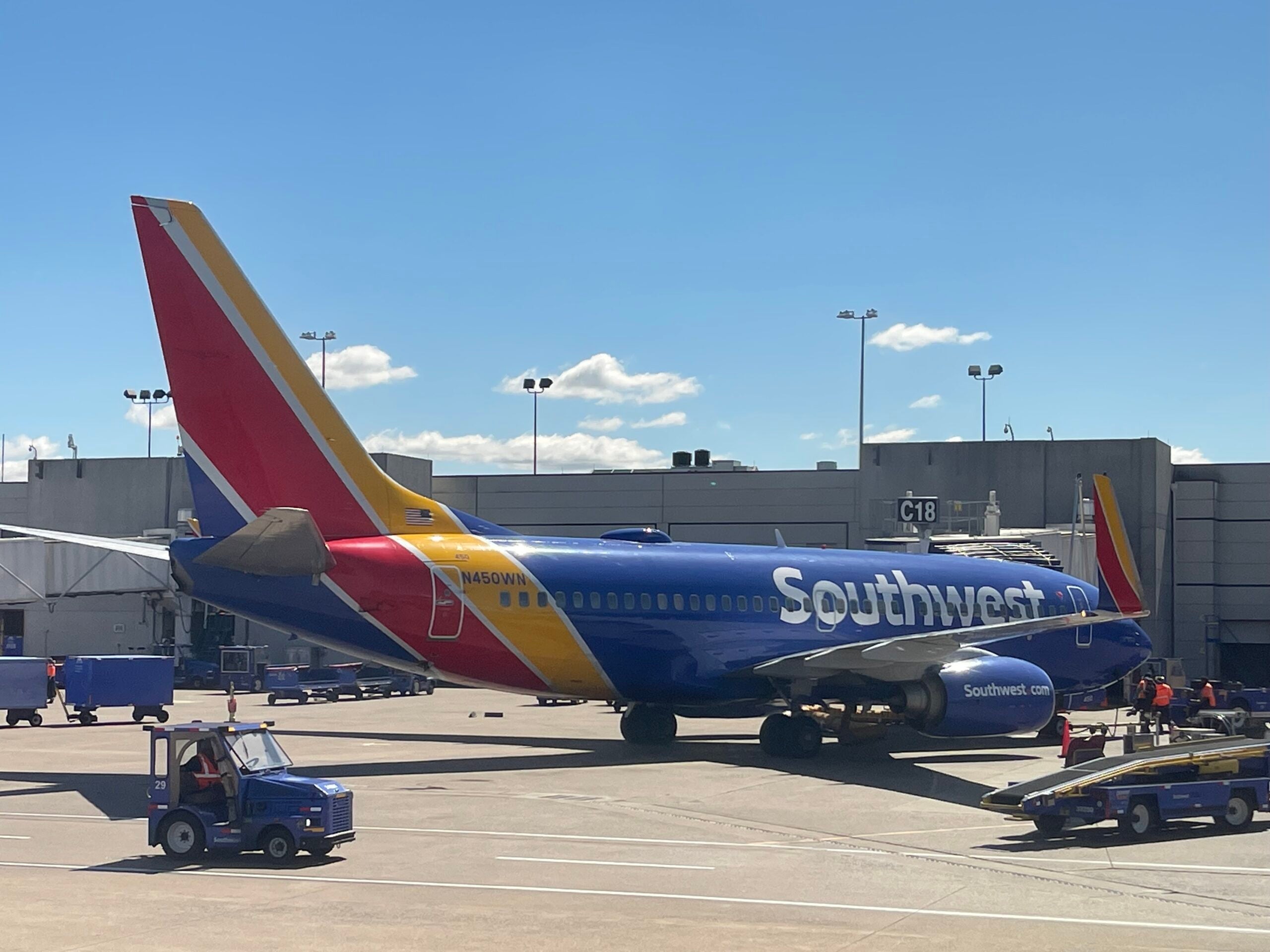 A blue Southwest Airlines Boeing 737-700 sits at an airport gate on a sunny day