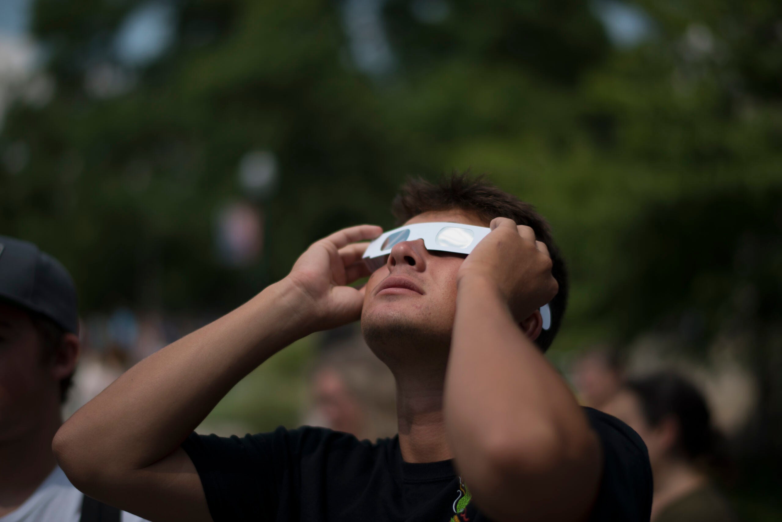 Young man looking up at solar eclipse wearing paper protective glasses