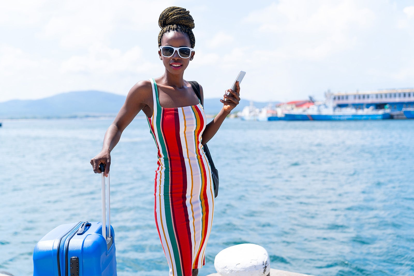 Woman with suitcase walking on harbor and talking on smart phone