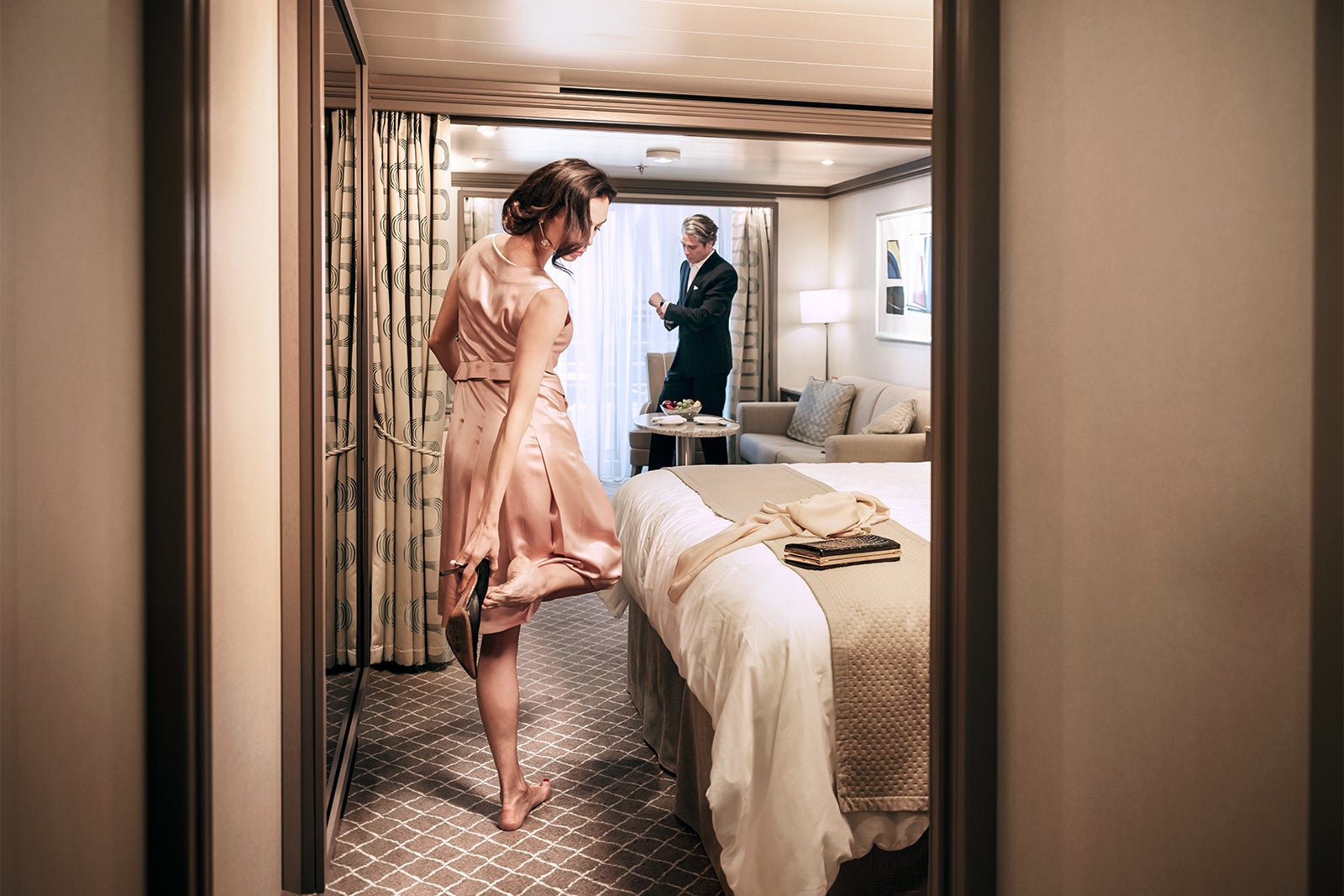 Lady putting on shoe and man straightening cuff link in cruise ship suite