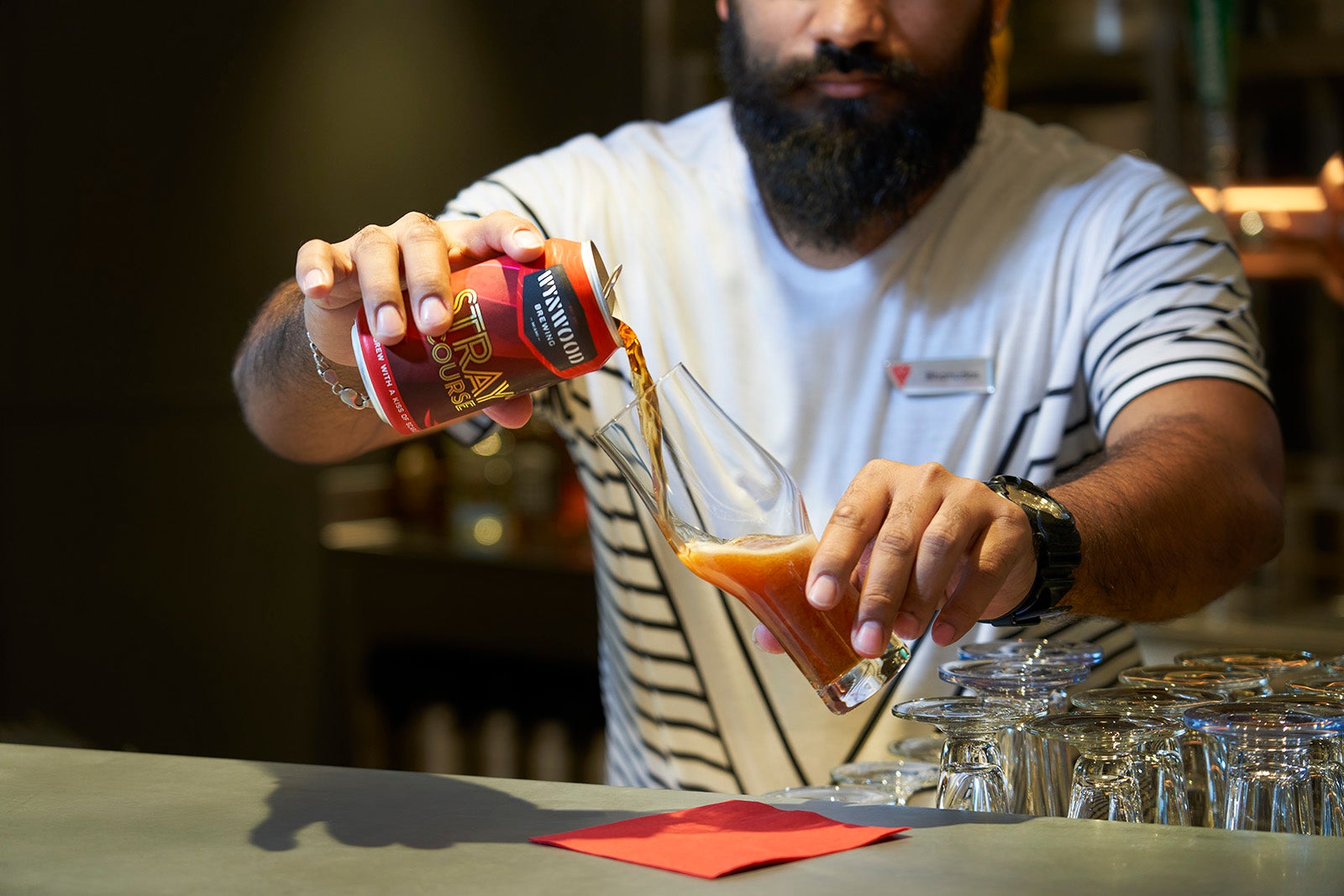 Bearded bartender pouring beer from a can into a glass