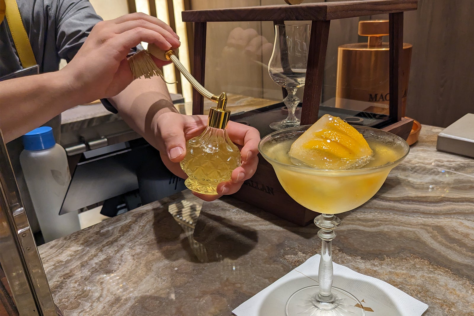 The bartender sprays an orange cocktail with aroma in a perfume bottle