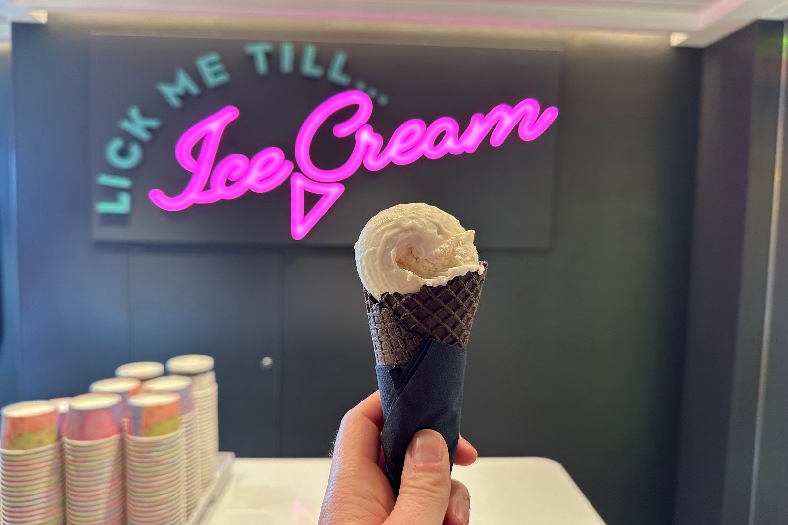 A hand holding a cone of ice cream in front of a neon sign