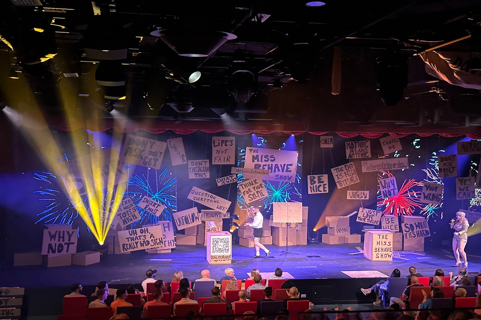 A cruise ship theater where the stage is filled with cardboard boxes during a game show