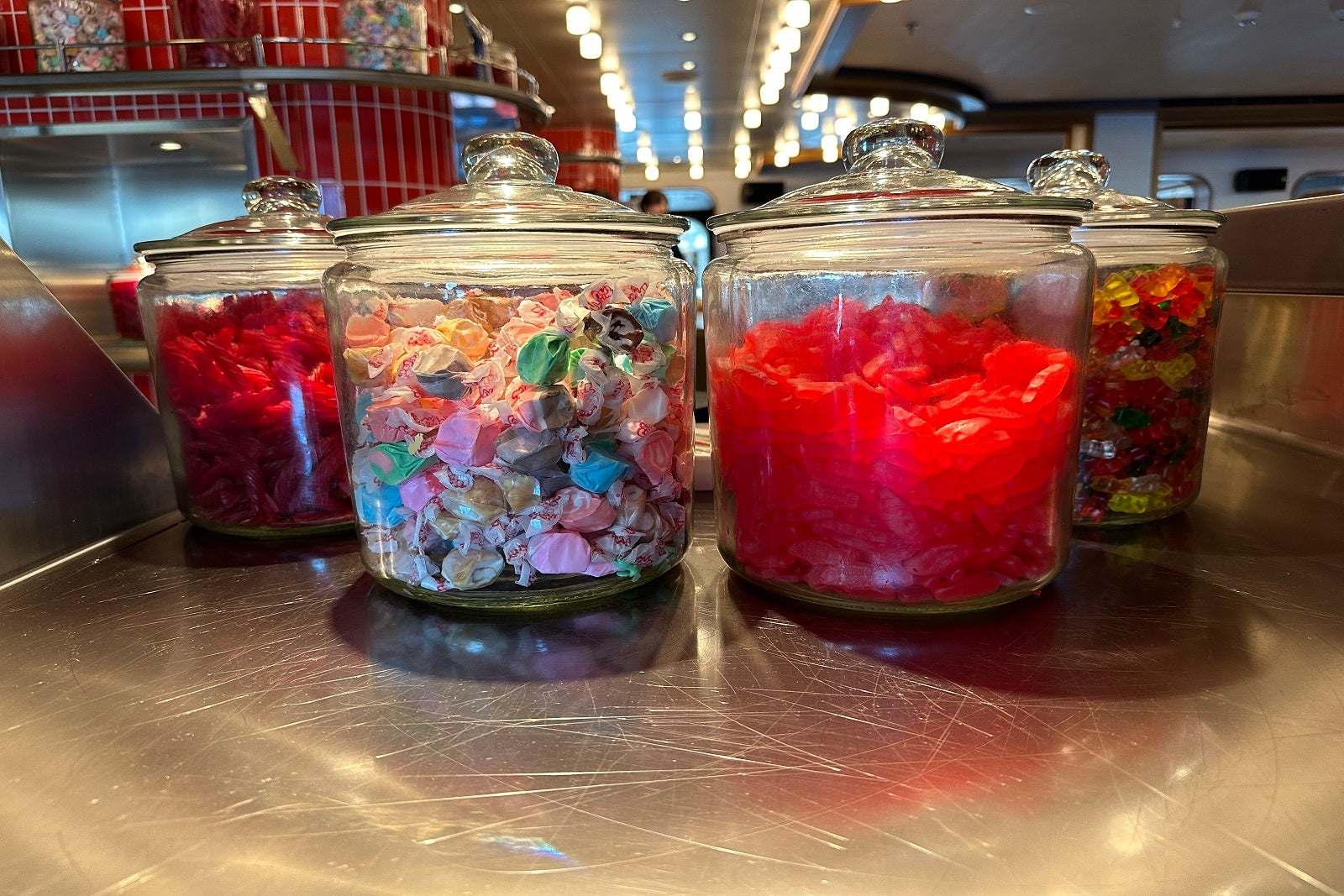 Four glass jars filled with Red Vines, saltwater taffy, Swedish Fish and gummy bears sitting on a counter