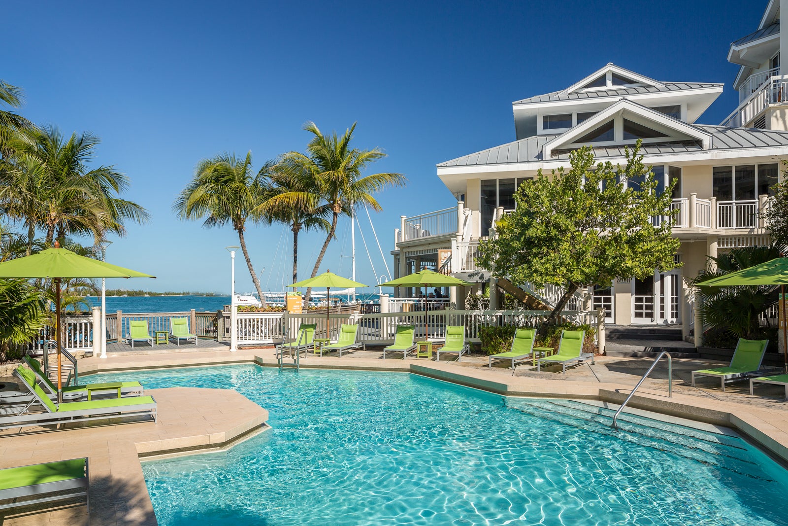 The outdoor pool at the Hyatt Centric Key West Resort and Spa is surrounded by green lounge chairs and palm trees.