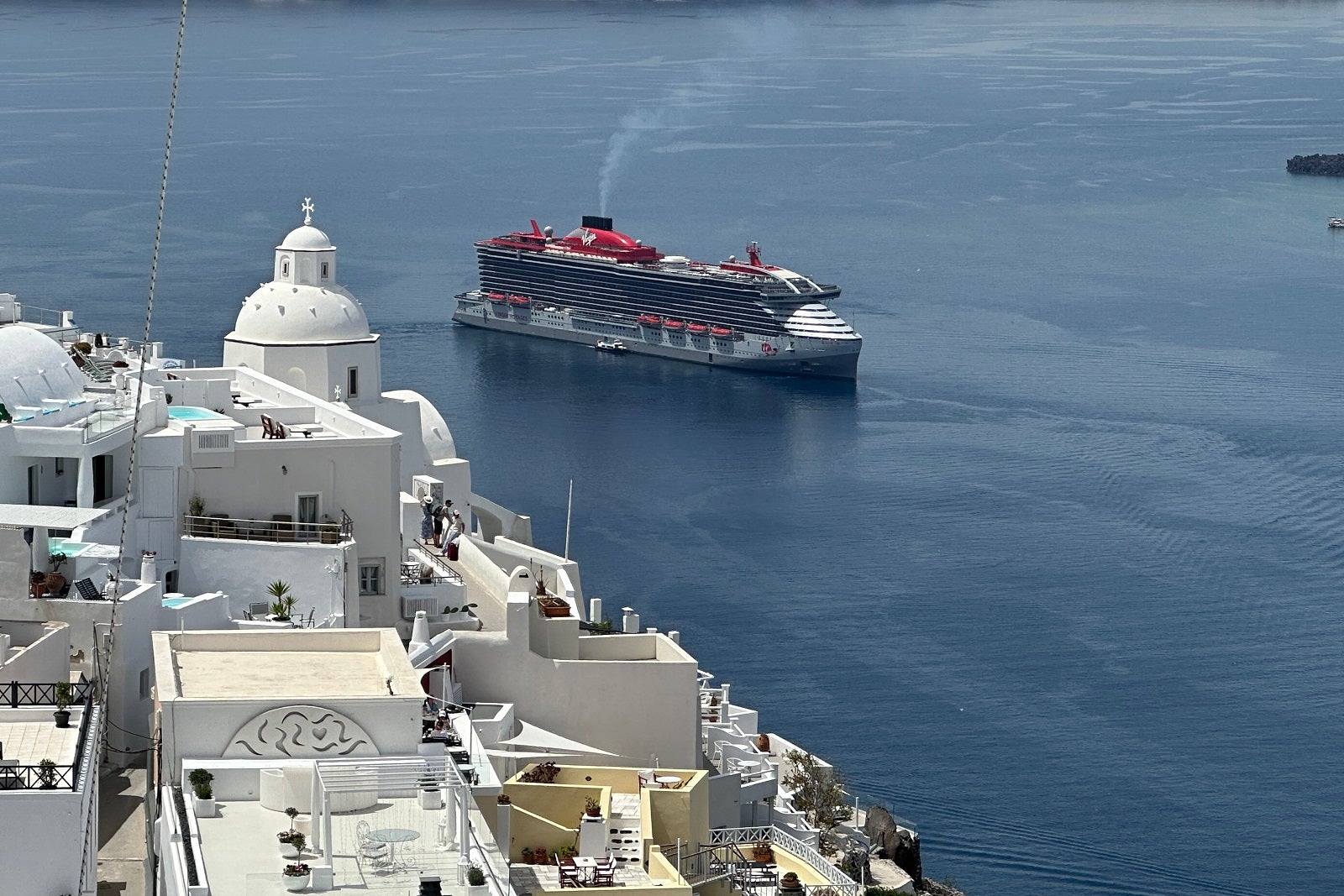 Virgin Voyages' Resilient Lady anchored off the shore of Santorini, Greece, with white buildings in the foreground