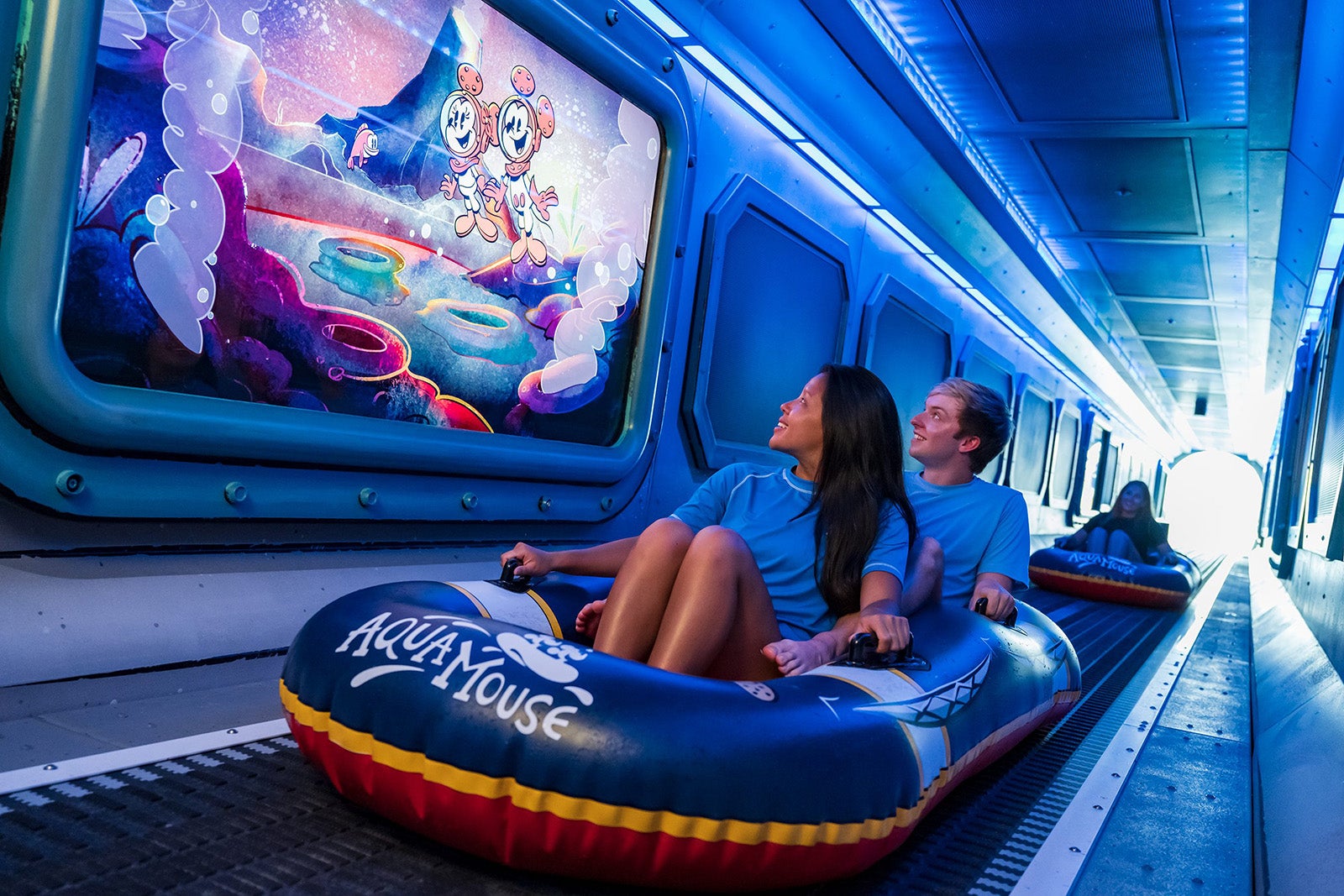 Two passengers sitting in a raft on a water slide watching a video screen