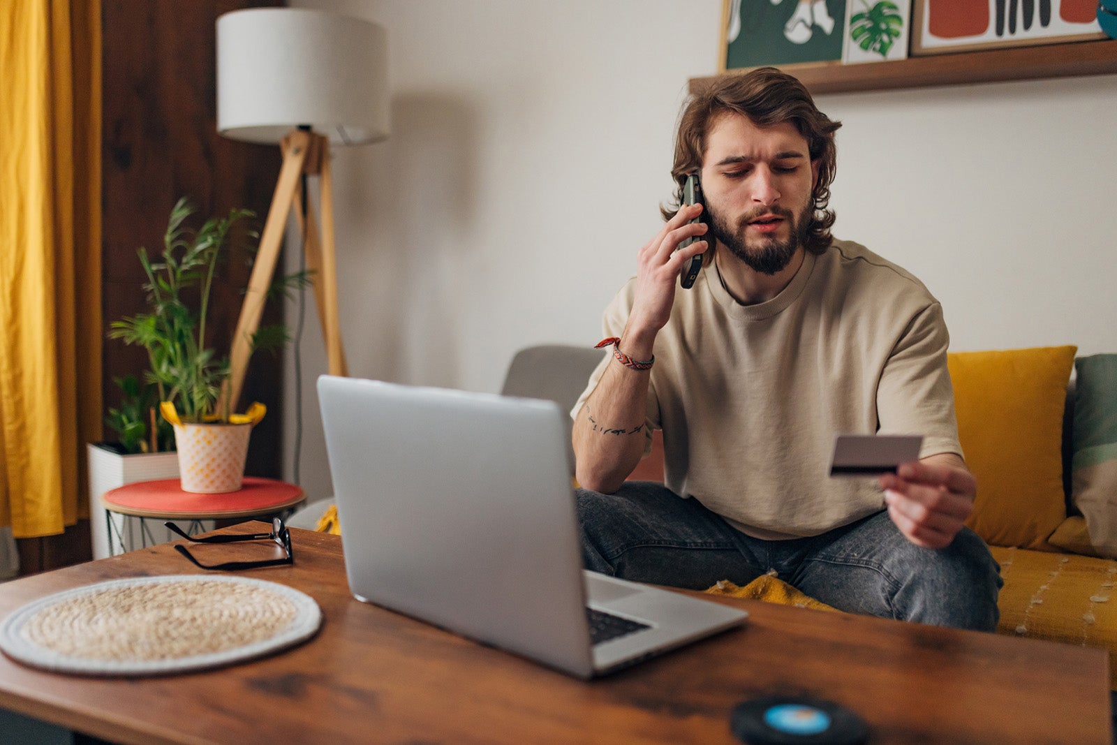 Man makes a phone call while trying to make an online purchase using a credit card and a laptop