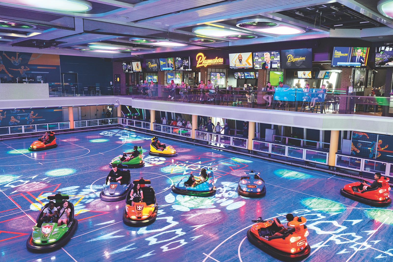 Teens in bumper cars on an indoor court on a cruise ship with a sports bar and a balcony overlooking the area