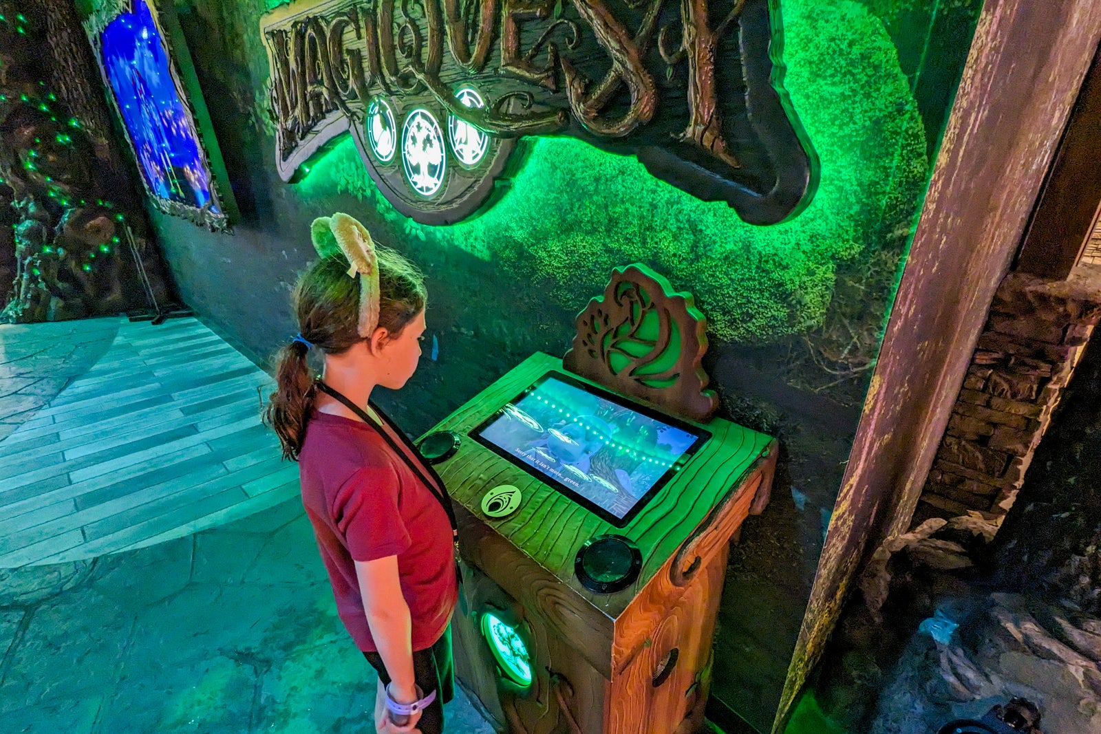 Girl with wolf ears headband looking at a screen under MagiQuest sign.