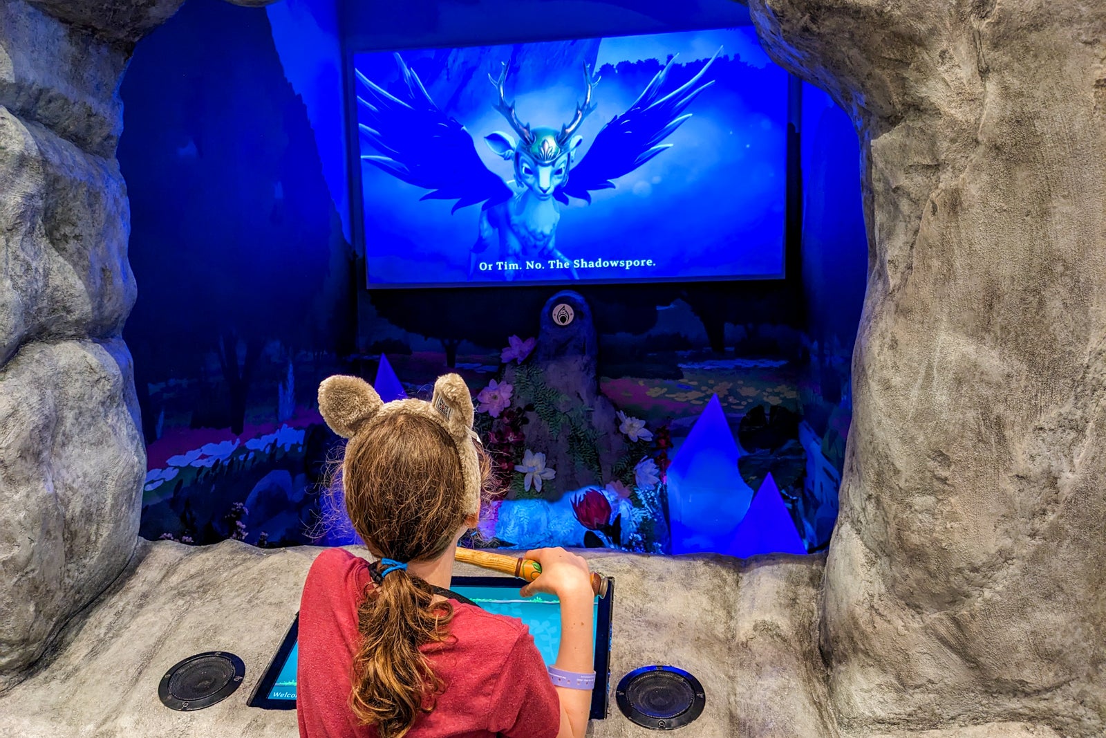 Girl wearing wolf ears headband watching animated characters on a screen