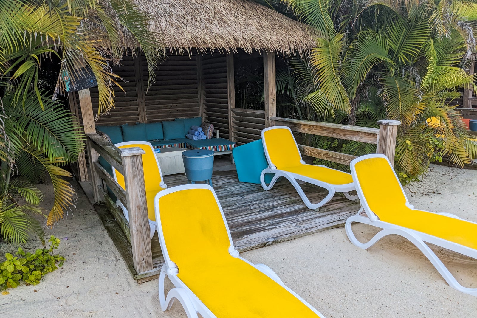 Thatched roof cabana with a couch inside and yellow lounge chairs in front