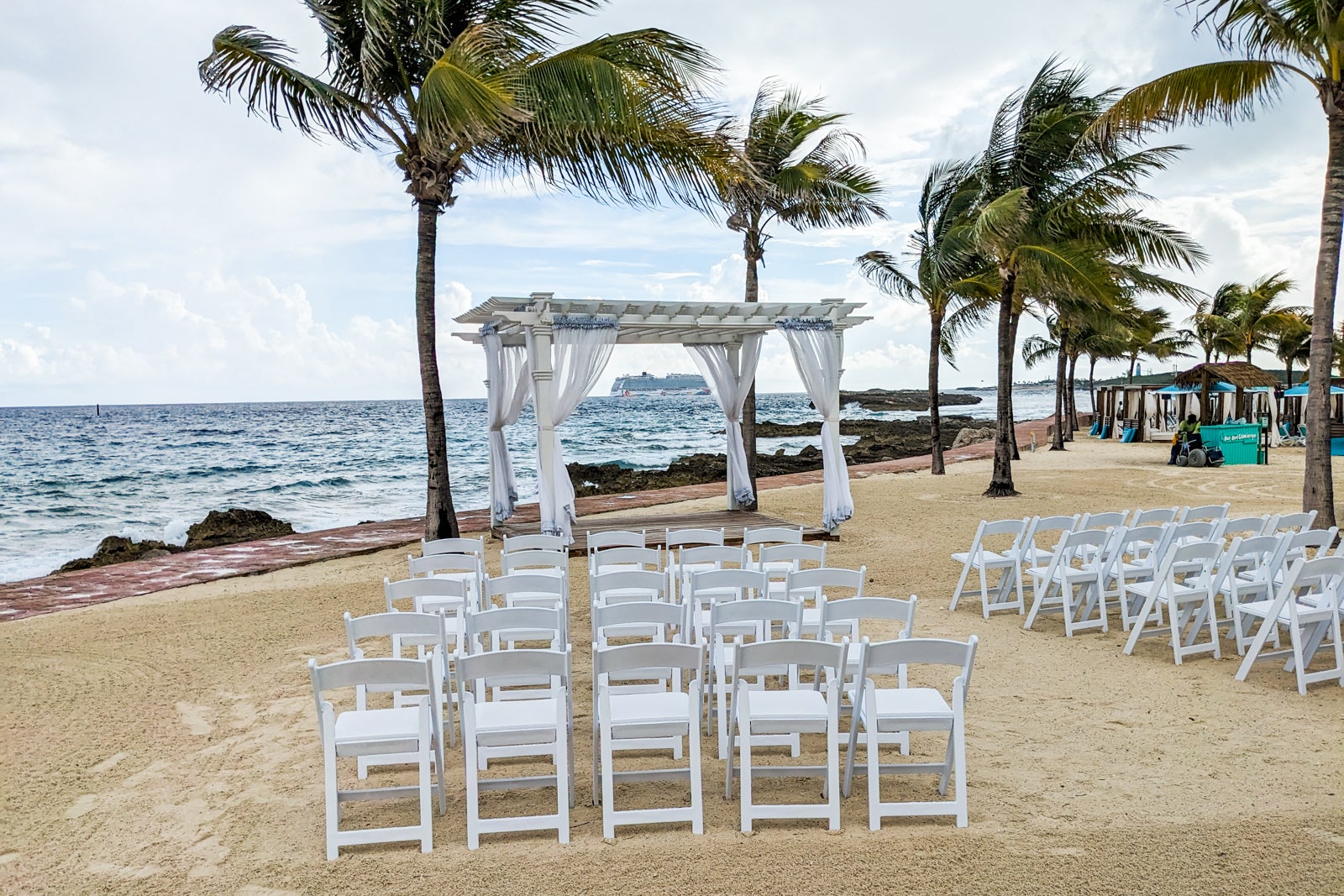 Beach wedding with white chairs, white draped canopy and palm trees