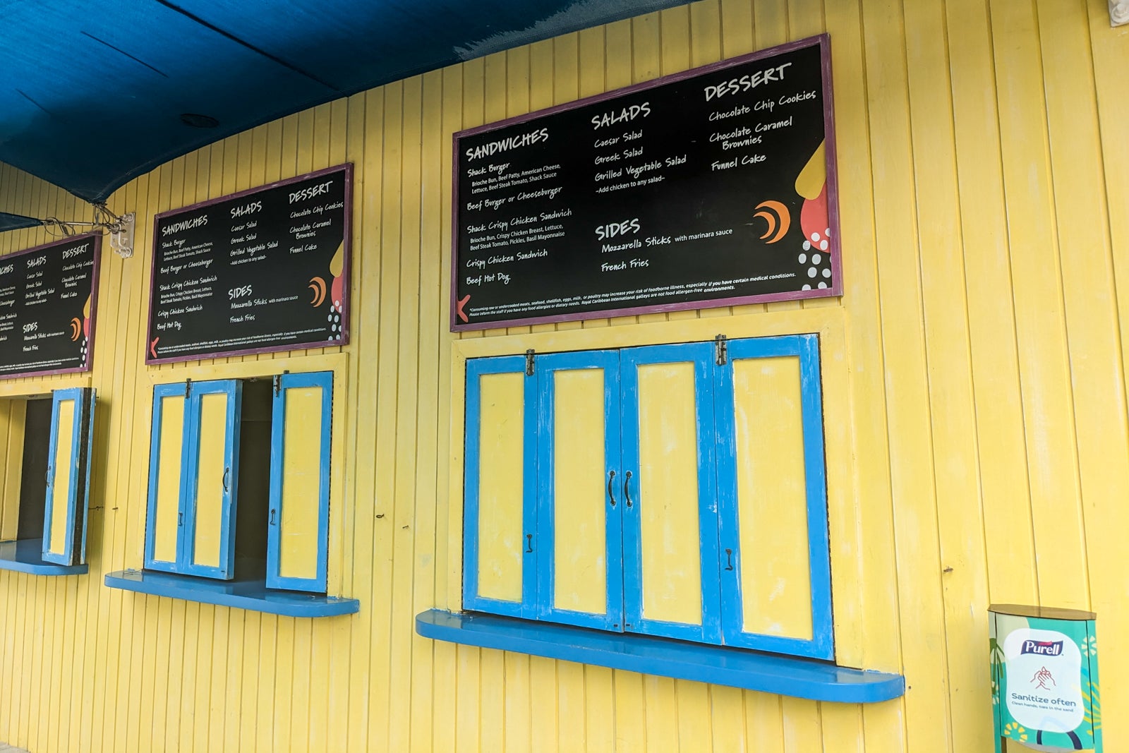 Yellow wooden shack with shuttered ordering windows and menu of burgers and sandwiches