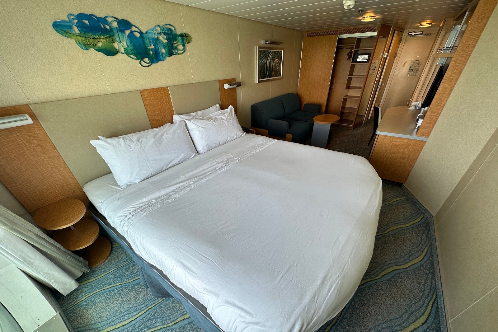 A cruise ship cabin with a queen bed, sofa and vanity