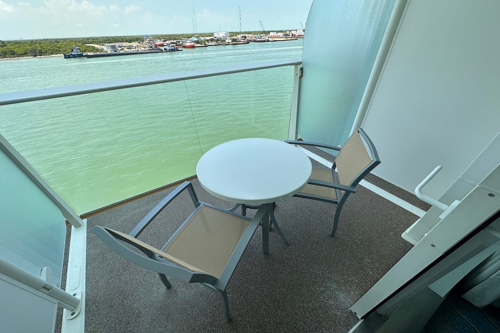 A cruise ship balcony overlooking the water, outfitted with two chairs and a table