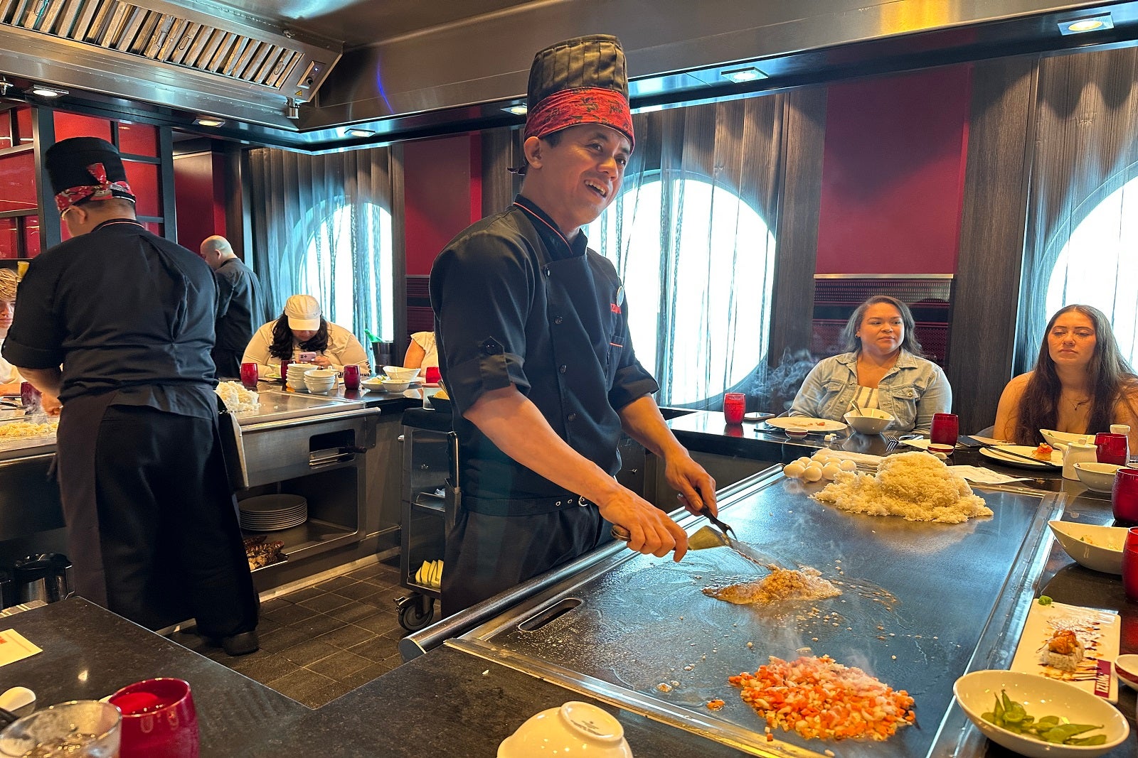 A chef cooking food at a cruise ship teppanyaki restaurant with people seated around a U-shaped table watching