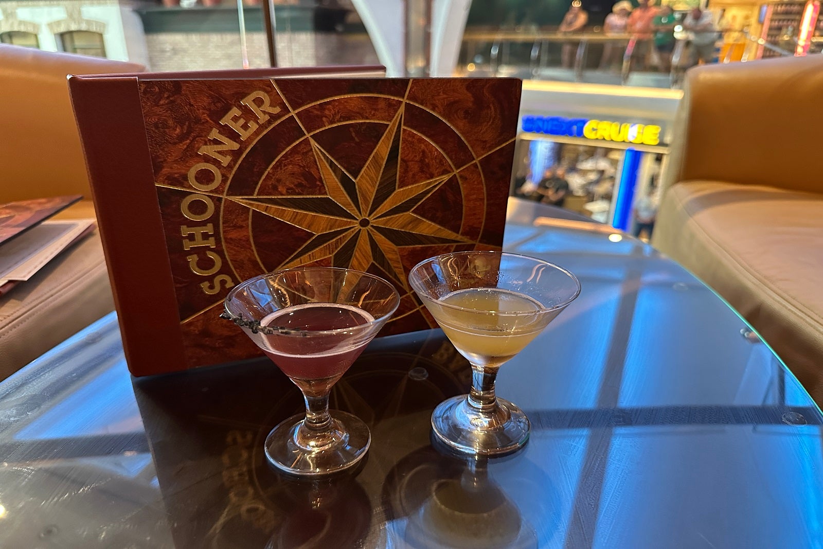 Two alcoholic drinks in miniature martini glasses on a table in front of a Schooner Bar menu