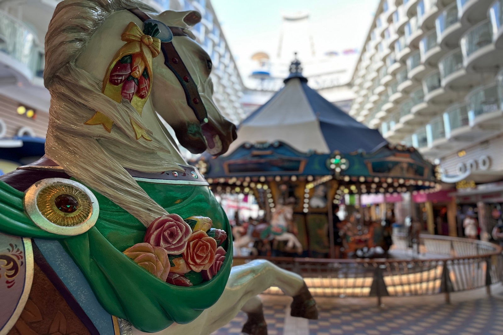 A carousel on an open-air boardwalk on a cruise ship with a carousel horse in the foreground