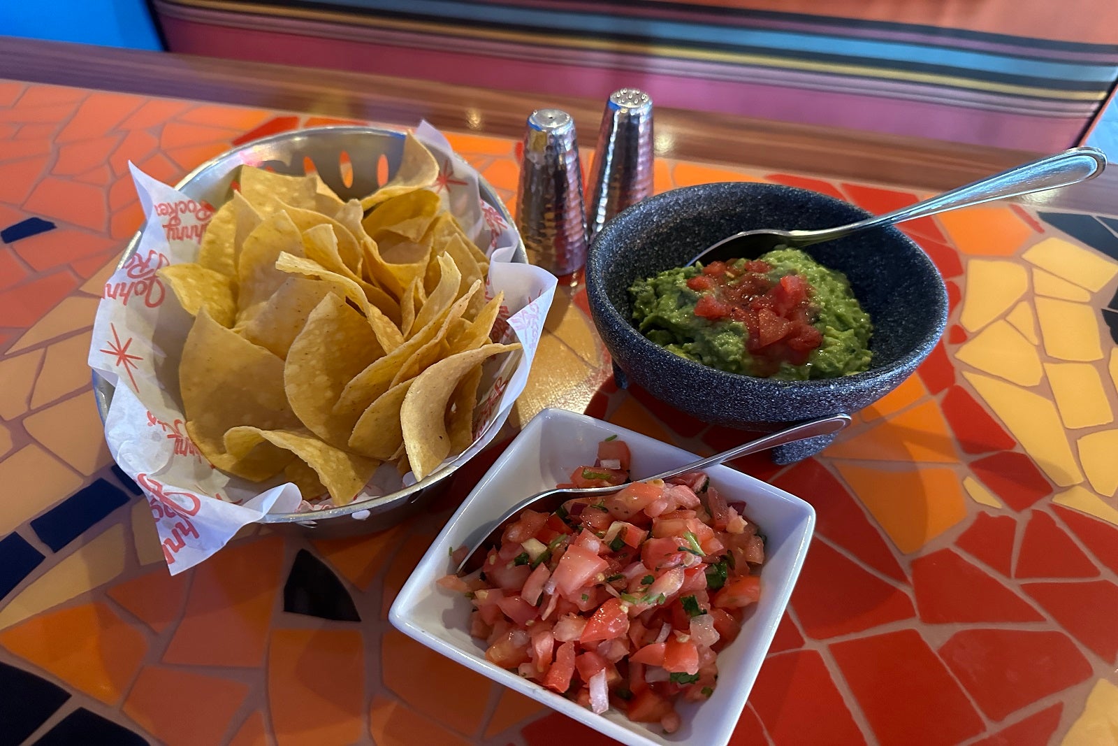 Bowls of tortilla chips, guacamole and salsa on a colorful mosaic table