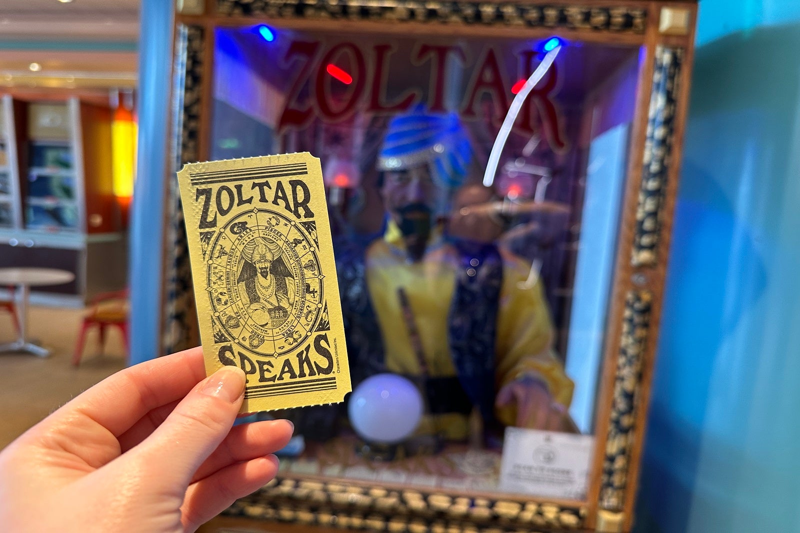 A hand holding a fortune ticket in front of a Zoltar fortune-telling machine