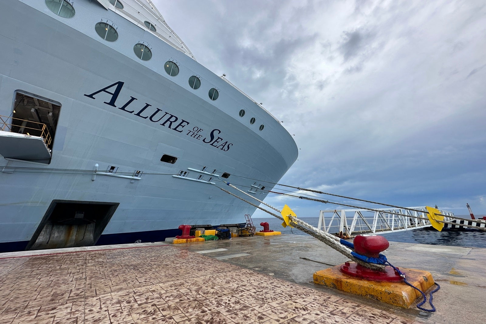 The front of a cruise ship tied up against a pier with the words "Allure of the Seas" on the hull