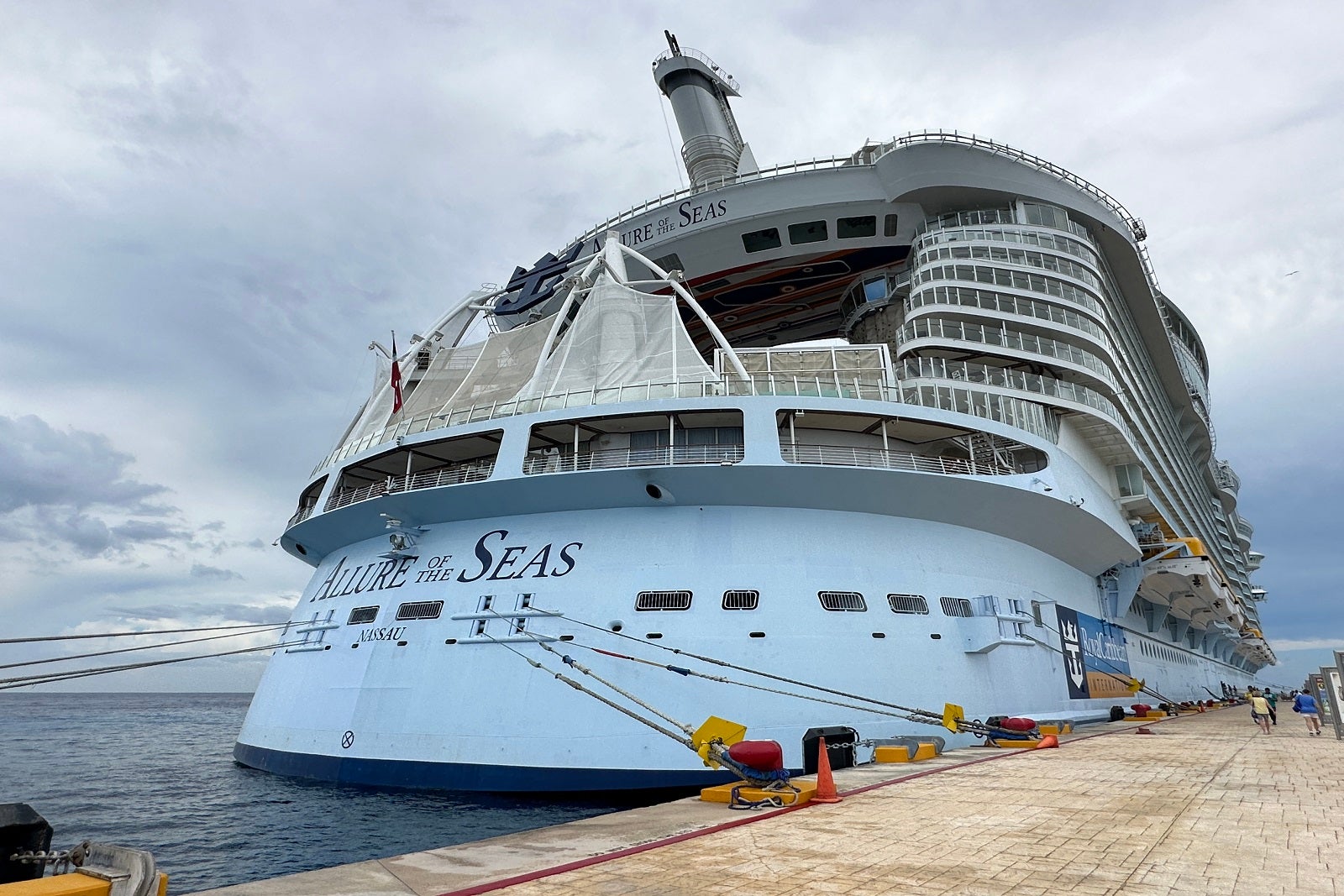 The aft of a cruise ship tied up at a dock with the words "Allure of the Seas" printed on the back