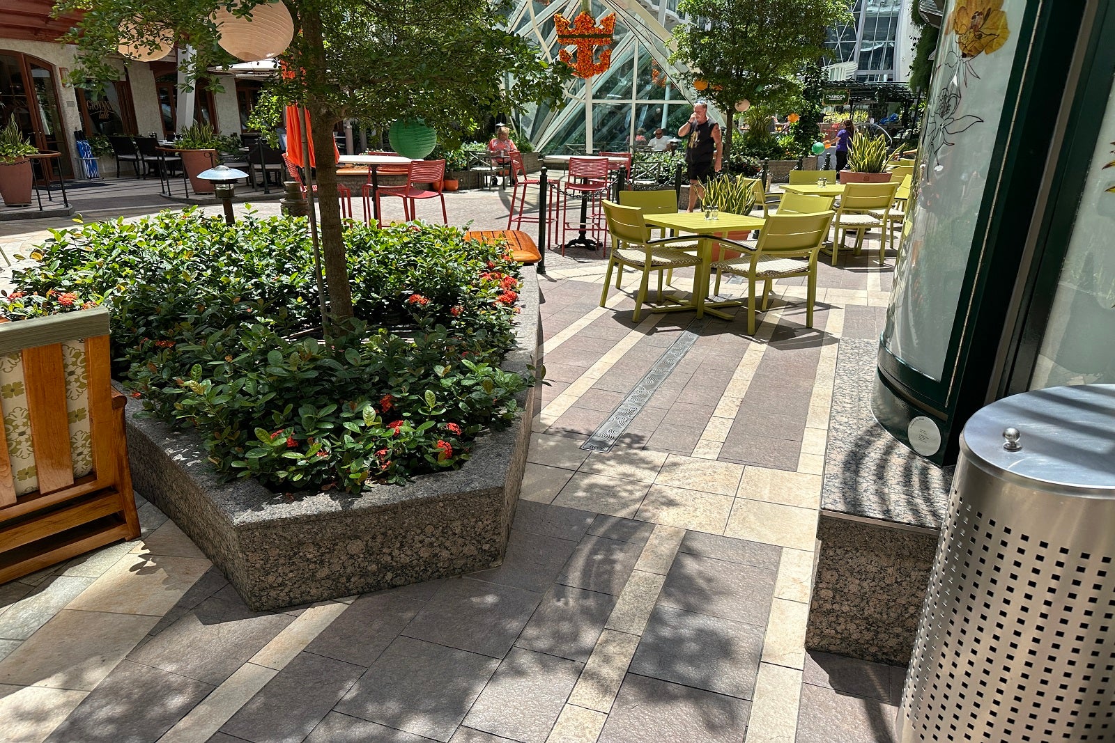 The seating area outside of a cruise ship restaurant along a sunny promenade with real plants