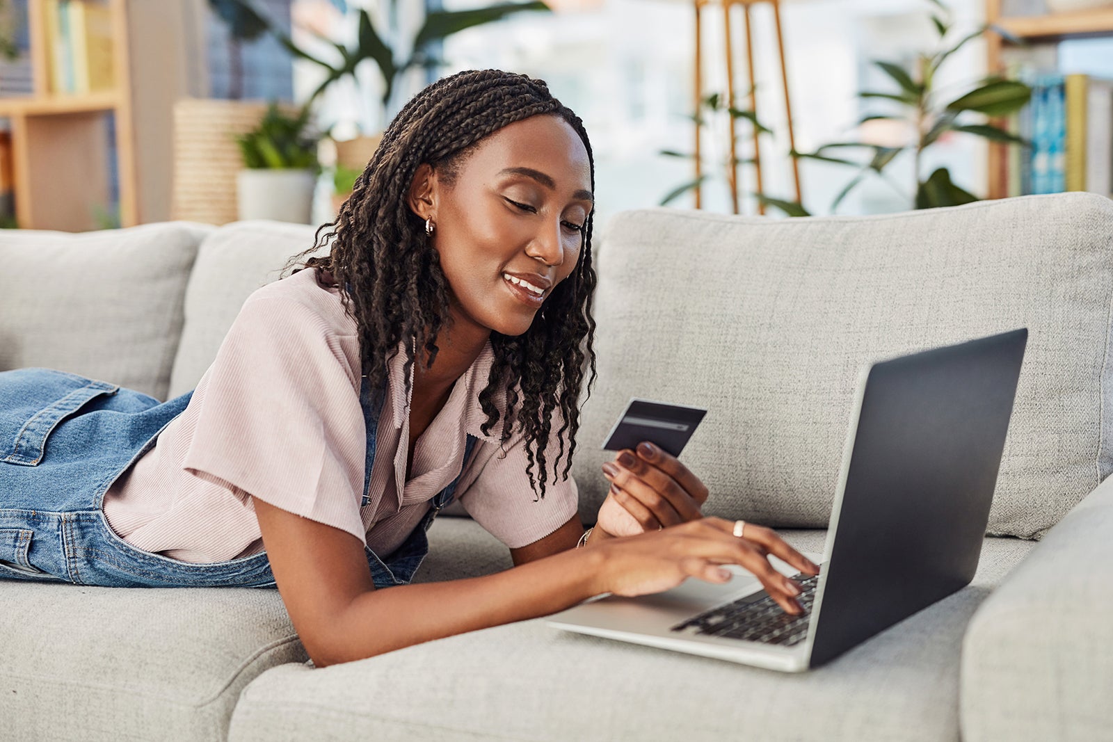 Online shopping, woman with laptop and credit card for payment on a sofa in living room of her home. Ecommerce, investment or pay bills and African female person with bank information for internet