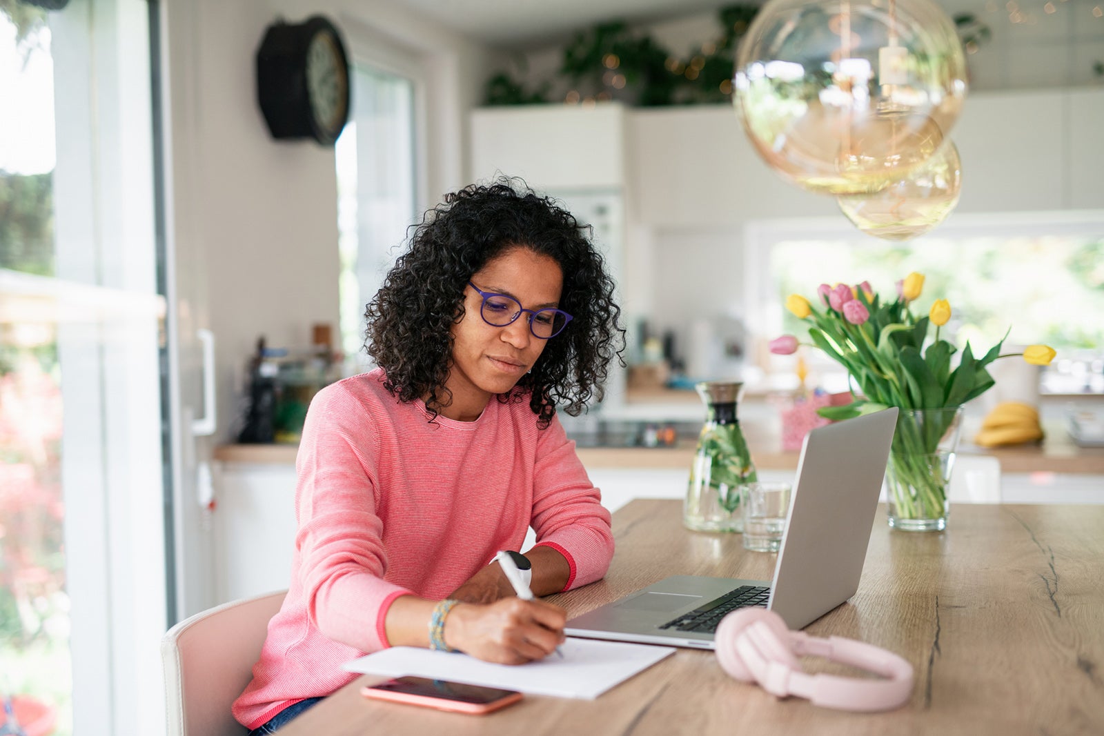 Woman writing something down in front of her laptop in her kitchen 