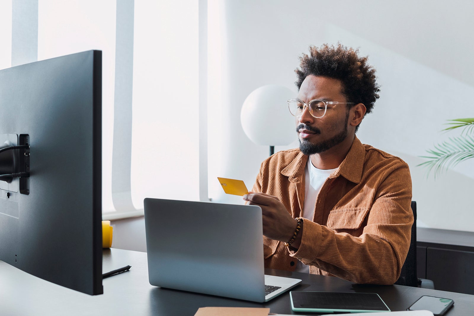 Um homem segura um cartão de crédito na mão enquanto está sentado em frente a um laptop