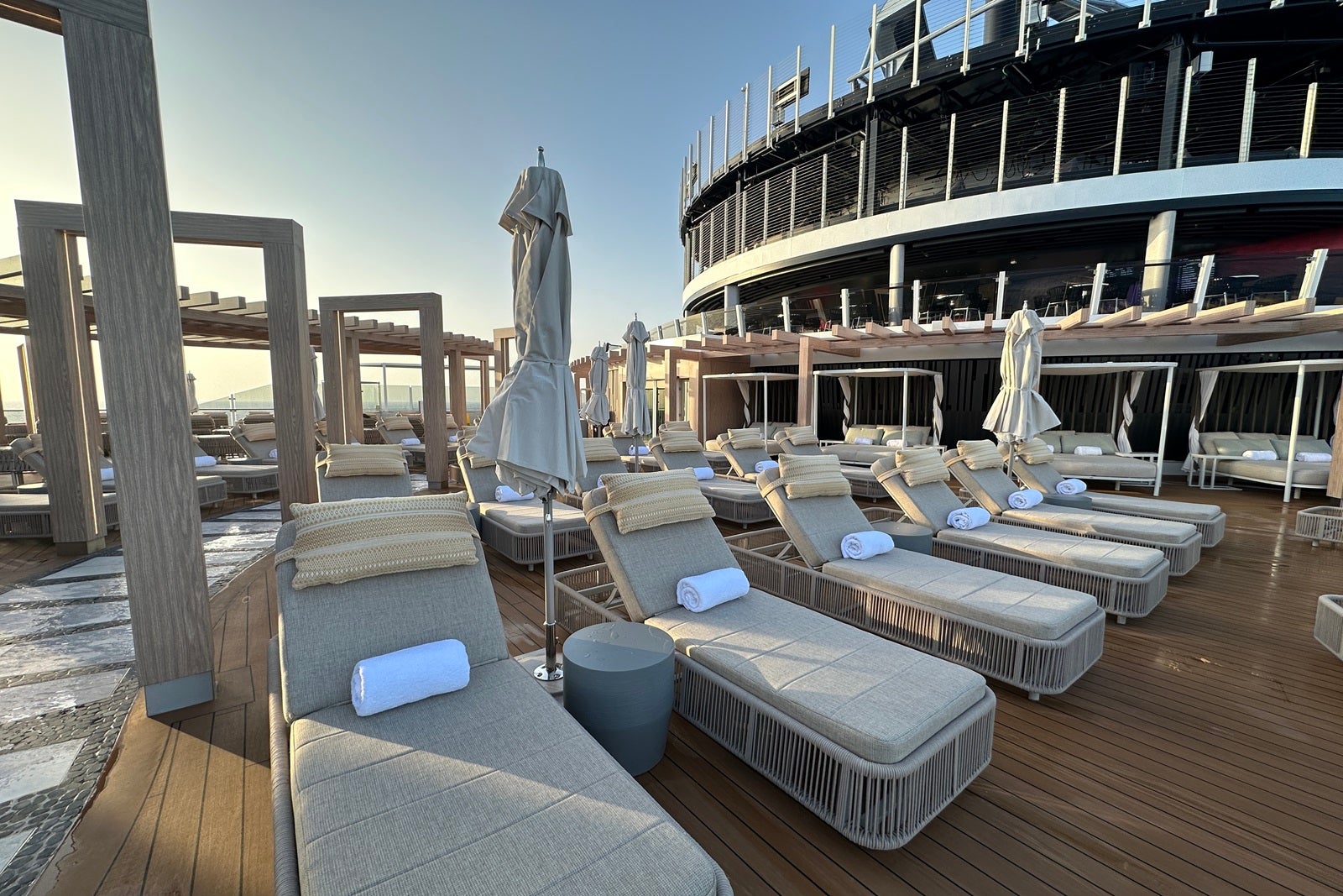 Rows of padded sun loungers in a row next to a walking path on a cruise ship sun deck